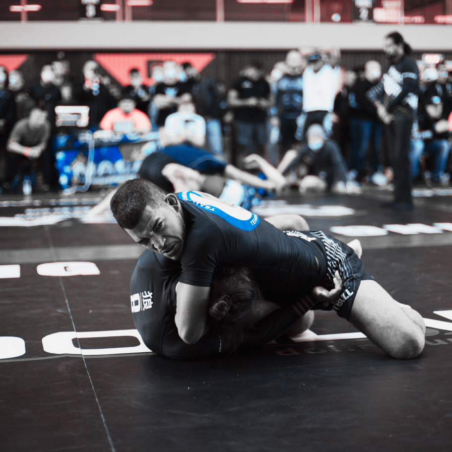 Zwei Kämpfer im Grappling, einer in schwarzer, der andere in blauer Kleidung.