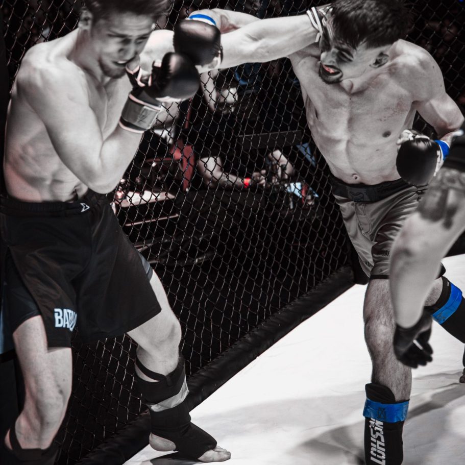 Zwei Kämpfer im MMA-Ring, einer schlägt mit einem rechten Hook zu.